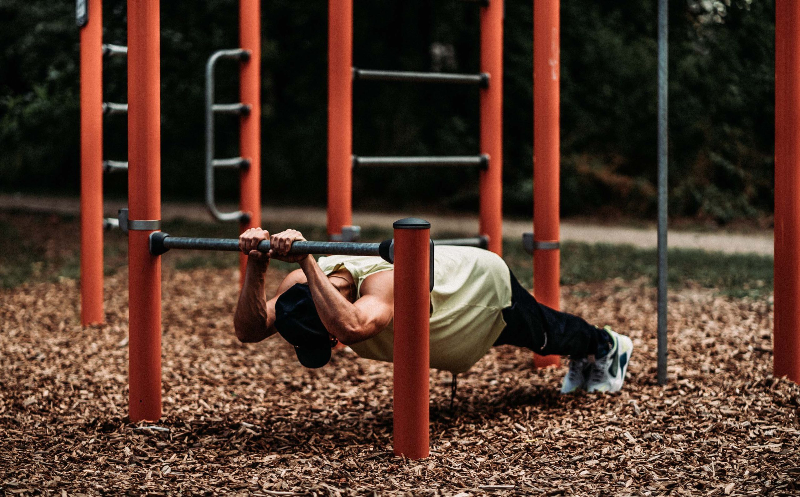 A man making use of an outdoor gym equipment by doing improvised planks. 
