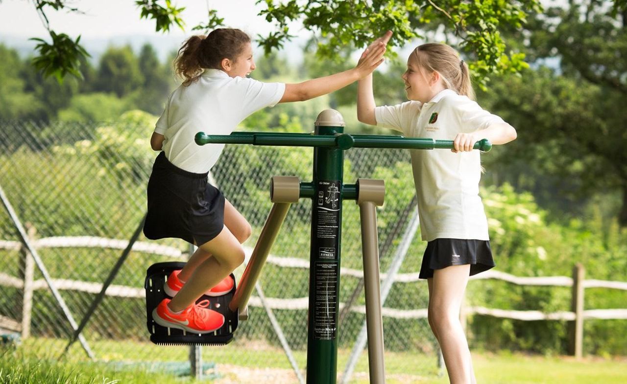 Two girls playing on an air skier at an outdoor playground.