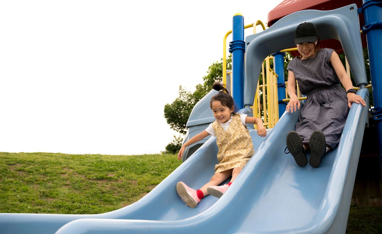 A woman and a girl sliding down a slide at an outdoor playground.