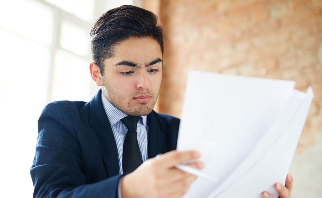 An Asian man going through a few sets of documents in an office.