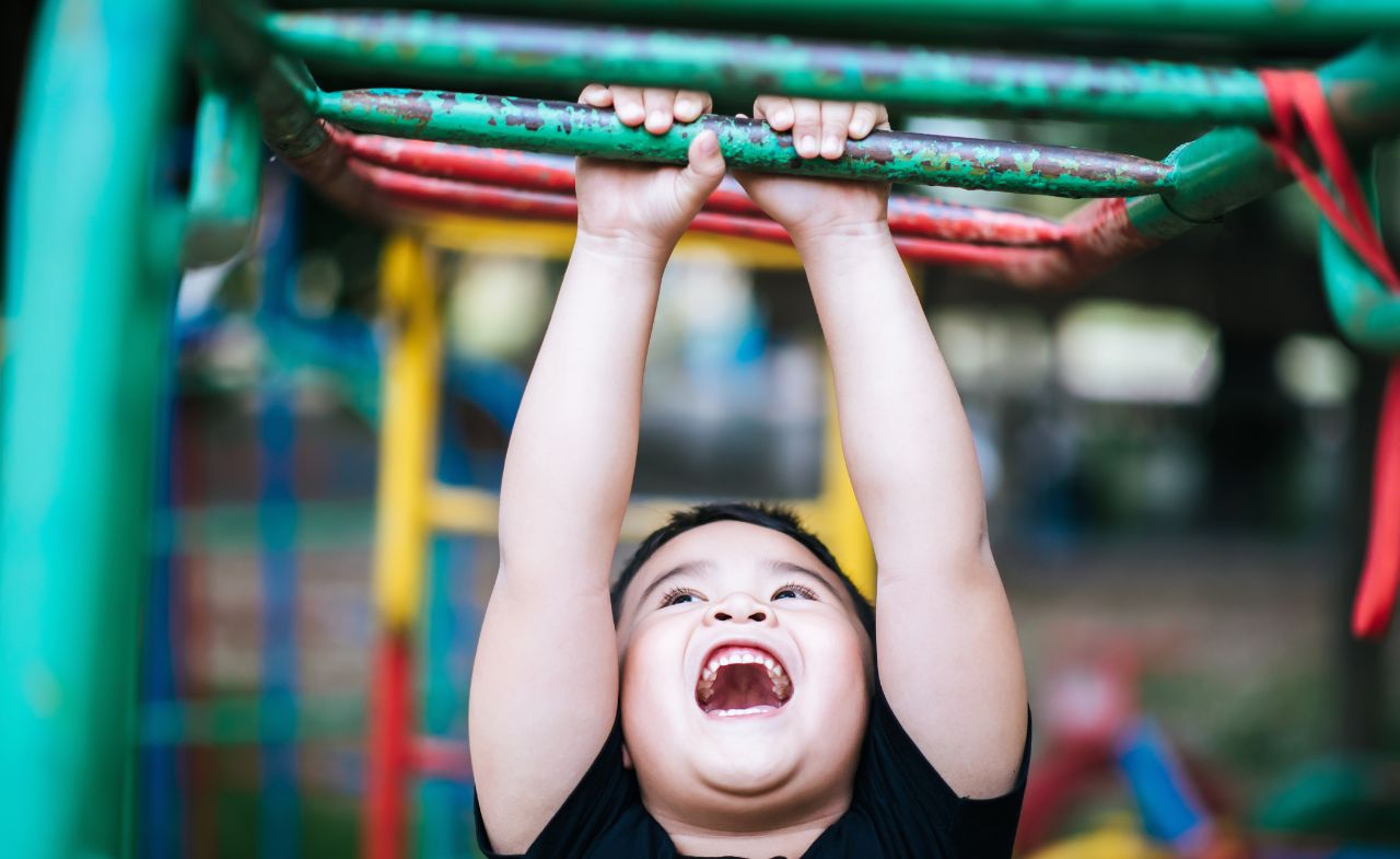 A boy smiling as he climbs on the monkey bar.