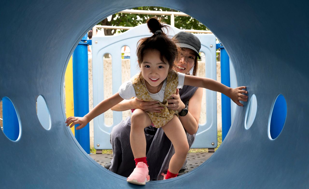 A woman holds a child by the waist as she explores a tunnel tube.