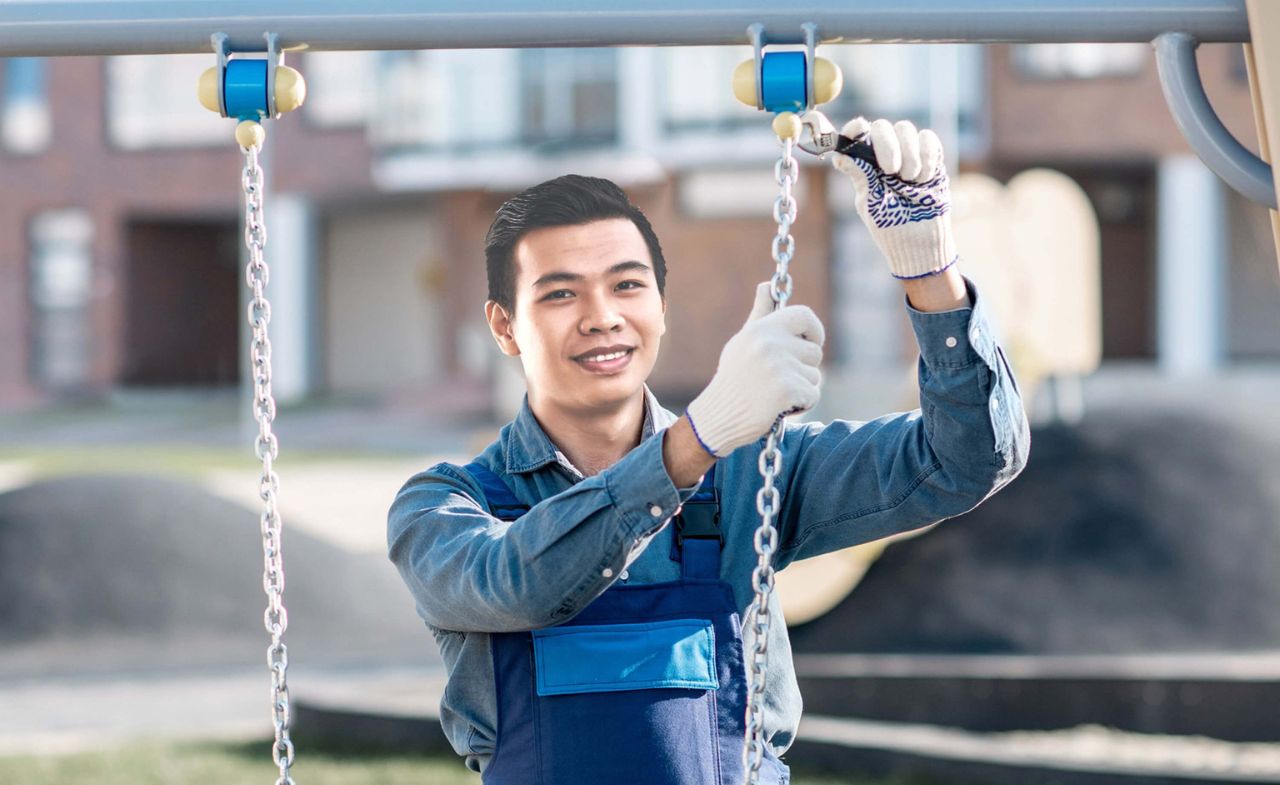 A playground contractor, performing maintenance on a swing to ensure it’s safe to be used.